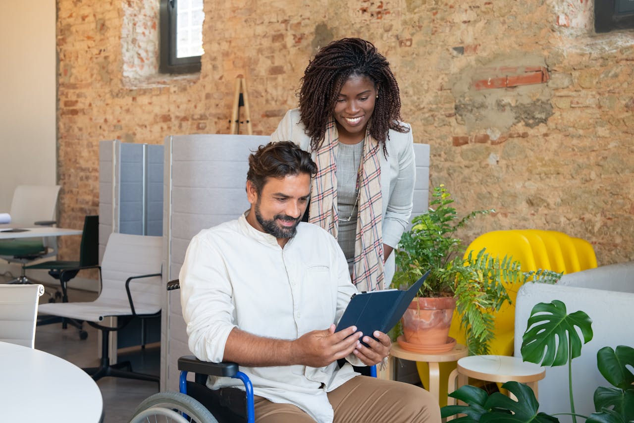 A Woman in Plaid Scarf Standing Beside the Man Sitting on Wheelchair